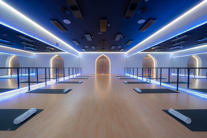 Modern yoga studio with soft lighting, wooden flooring, yoga mats, and mirrored walls.