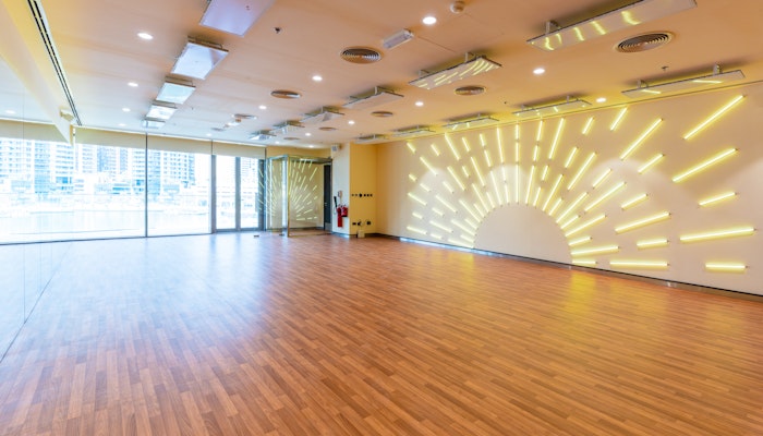Fitness First, Marina Gate Empty fitness studio featuring wooden floors, large windows with city views, and a wall with sunburst LED lighting.