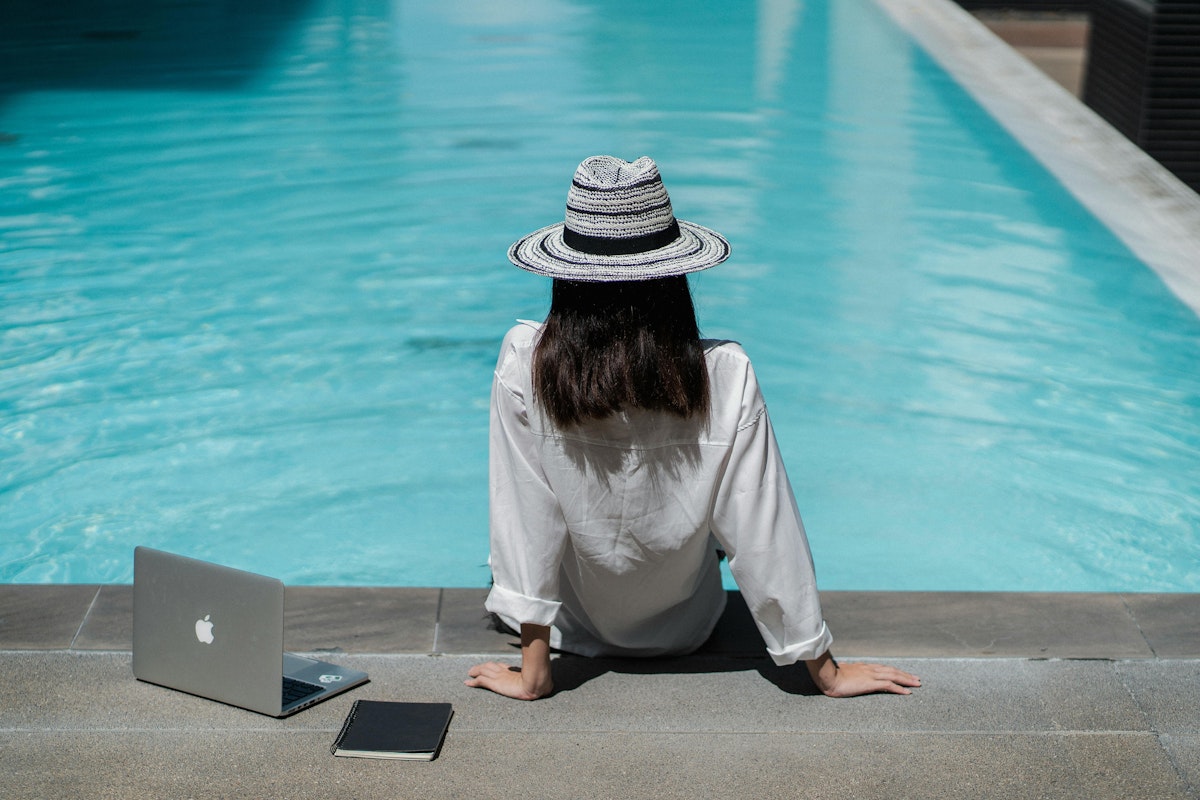 A woman relaxing by a pool, working on her laptop as part of a corporate wellness initiative, blending professional tasks with a serene outdoor setting