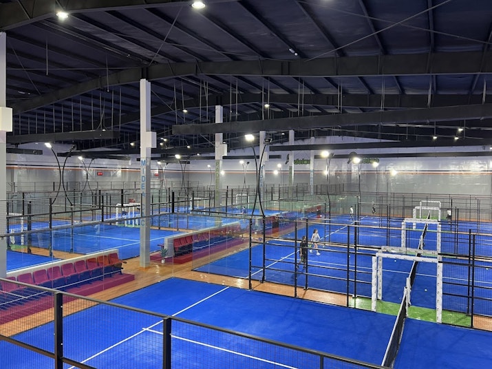 Indoor padel courts with blue flooring and seating area.