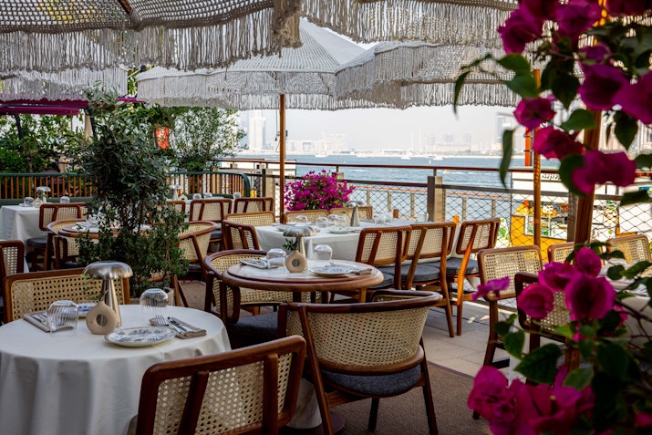 Outdoor seating with set for dining, lush greenery with a scene waterfront view