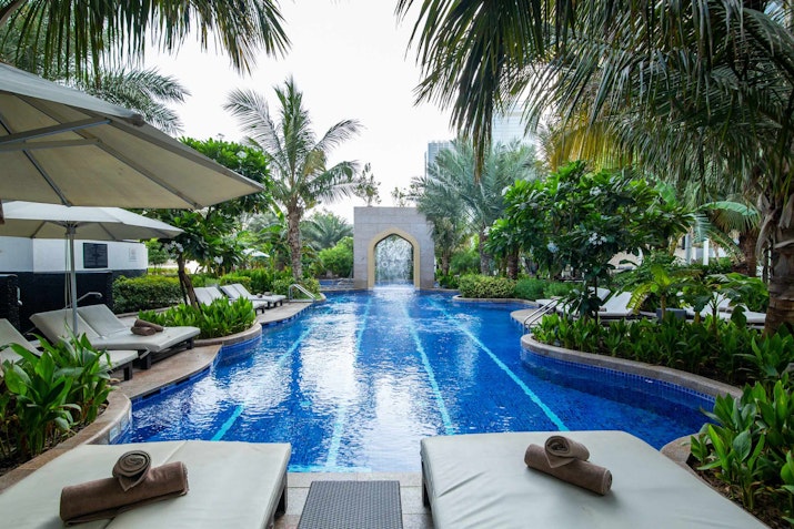 Long pool with sun loungers surrounded by palm trees and other greenery.
