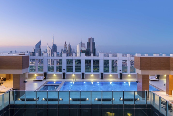 A rooftop pool with city views at sunset, showcasing skyscrapers and a luxurious atmosphere.