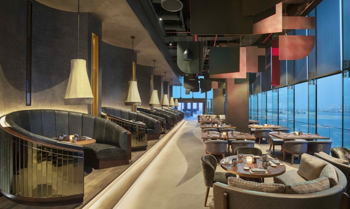Elegant, modern interior of Akira Back restaurant at W Dubai - The Palm, featuring plush seating, ambient lighting, and large windows with waterfront views.