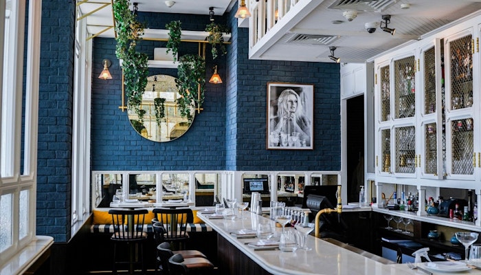 BB Social Dining in DIFC Interior of BB Social Dining in DIFC, featuring a stylish bar area with dark blue walls, white cabinetry, contemporary decor, and indoor plants adding a fresh touch to the modern setting.