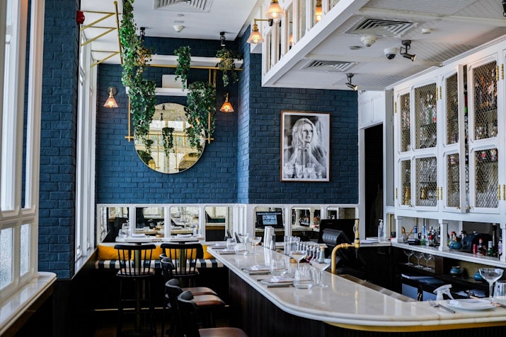 Interior of BB Social Dining in DIFC, featuring a stylish bar area with dark blue walls, white cabinetry, contemporary decor, and indoor plants adding a fresh touch to the modern setting.