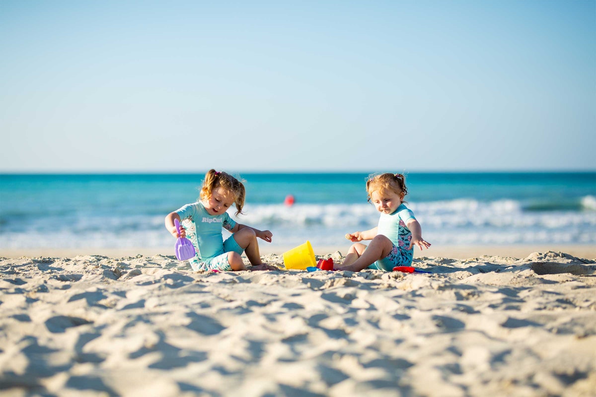 Two young children playing with sand toys on a sunny beach