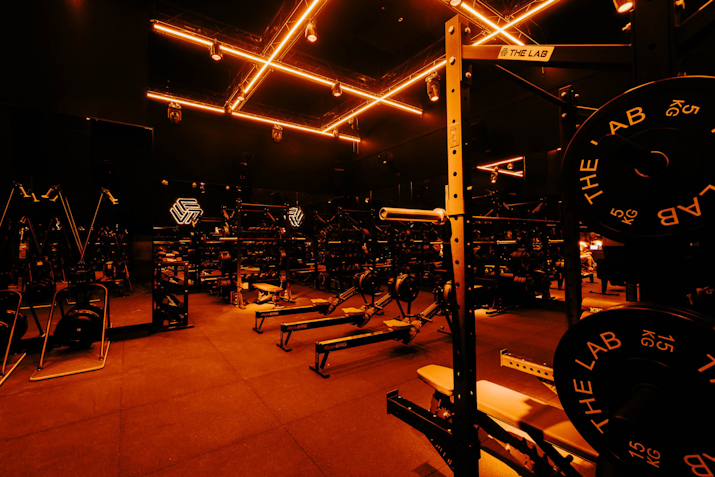 Dark fitness studio equipped with squat racks, resitance machines, and free weights