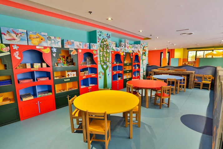 Bright and colorful children’s playroom with small tables, chairs, and shelves filled with books and toys