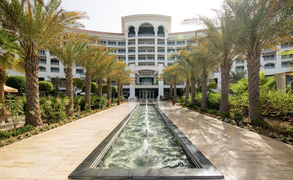 A pathway with palm trees leading towards a building, with a fountain flowing through the center.