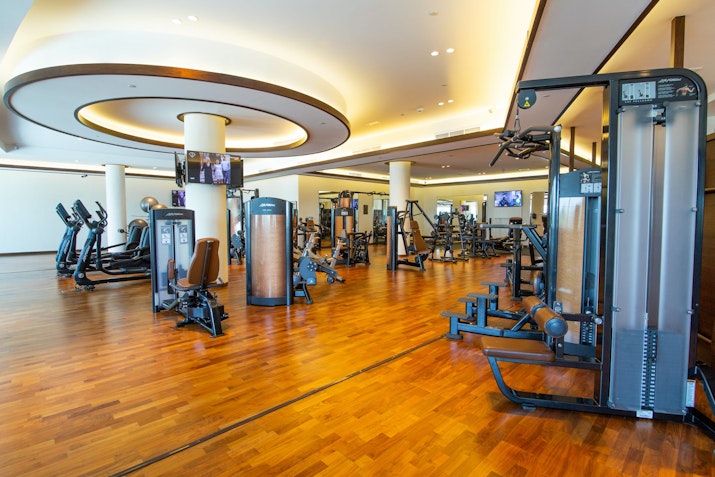 A spacious gym with various fitness equipment and wooden flooring.