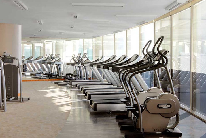 A modern gym interior featuring multiple elliptical machines and cardio equipment with large windows allowing natural light