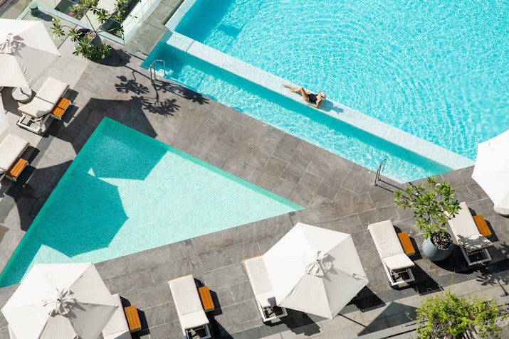 InterContinental Dubai Marina Aerial view of a pool area with lounge chairs and umbrellas, featuring a person relaxing in the water.