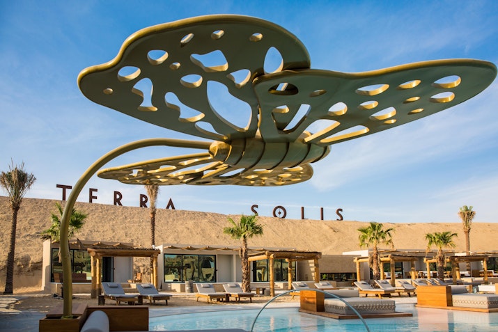 Modern outdoor poolside area featuring decorative shade structures and comfortable seating under a blue sky