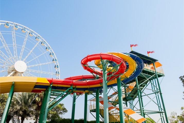 Brightly colored water slides with twists and turns, located near a large Ferris wheel under a blue sky