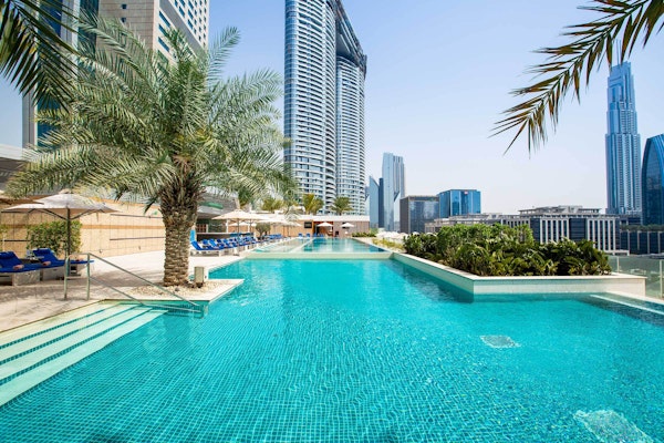 Rooftop pool with palm trees and skyscrapers in the background.