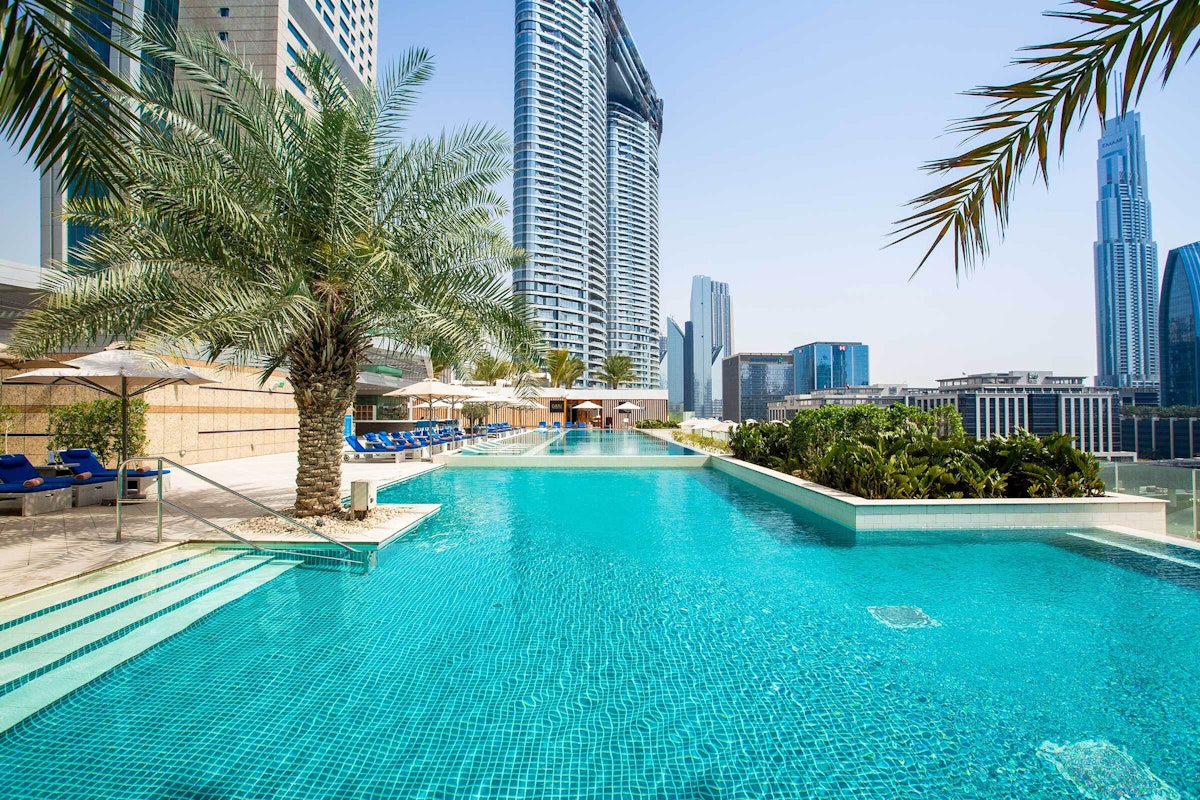 Rooftop pool with palm trees and skyscrapers in the background.