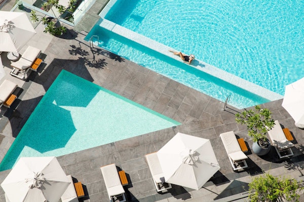 Aerial view of a pool with a person lounging under an umbrella.