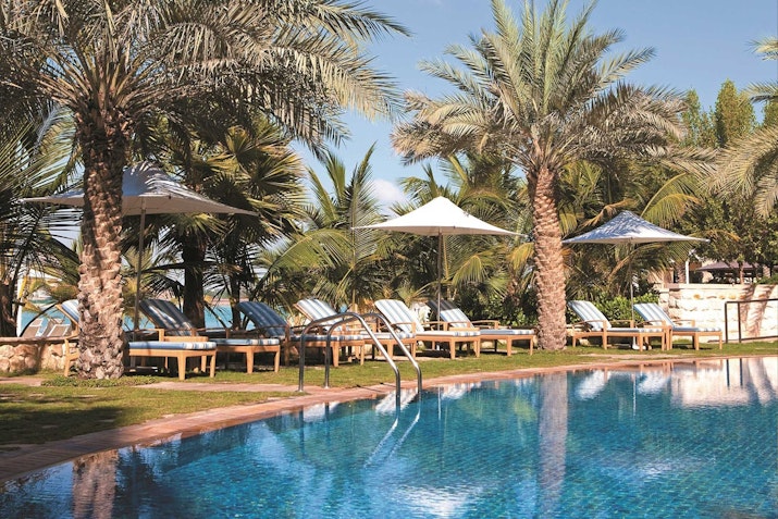 A serene poolside scene with lounge chairs and umbrellas surrounded by palm trees.