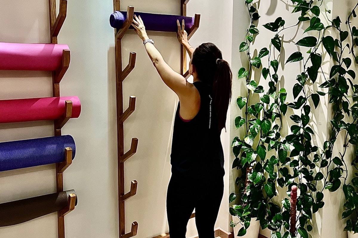 Your Zen at Yoga Ashram Person placing a yoga mat on a rack in a fitness studio