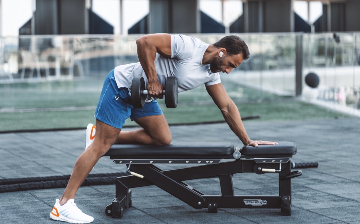 Man doing a workout with a dumbbell on a bench at a gym.