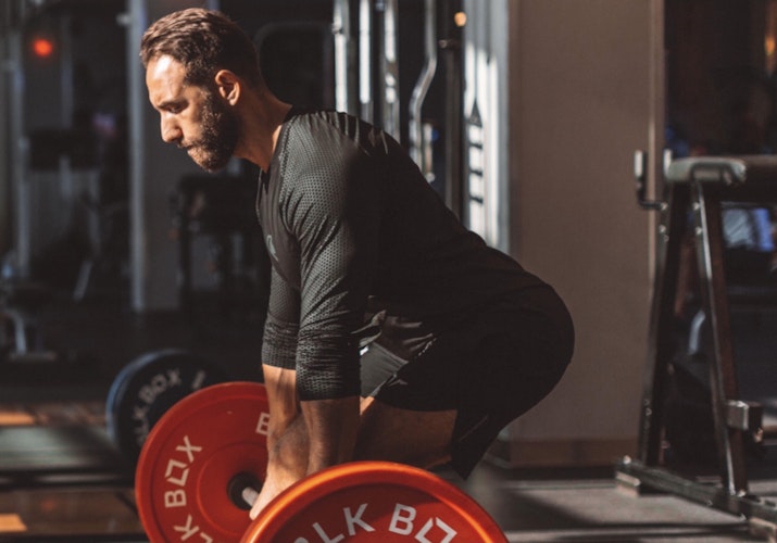 Man performing deadlifts in a gym with weights on a barbell.