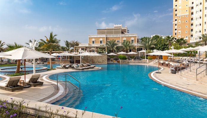 Soluna Beach Club A scenic view of a hotel pool area with sun loungers, umbrellas, and palm trees under a blue sky.