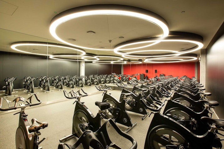 A fitness studio with multiple stationary bikes arranged in rows under circular lighting.
