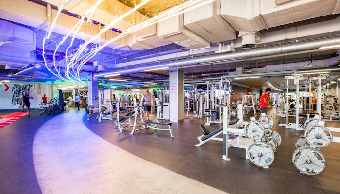 FitRepublik A spacious gym interior featuring various weightlifting equipment and colorful LED lighting, with individuals exercising in the background.