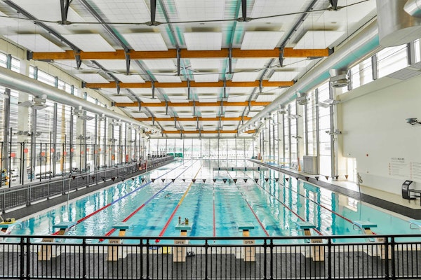 An indoor swimming pool with multiple lanes, large windows, and high ceilings.