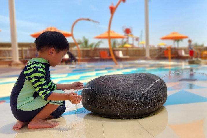 A child in a swimsuit playing with a water fountain at a water park.