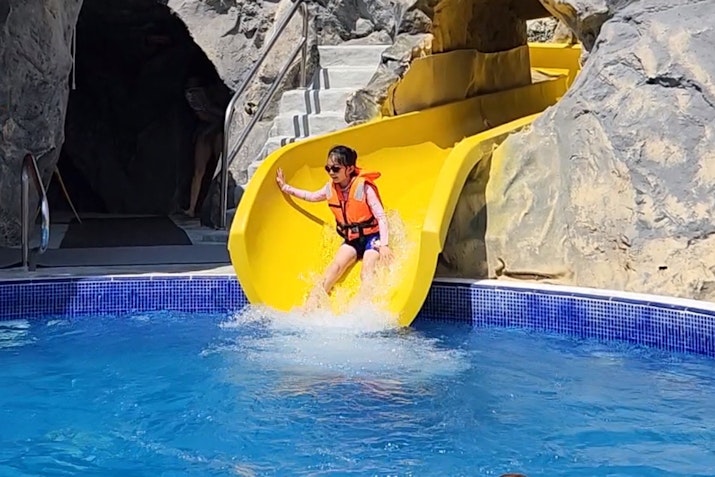 Child wearing a life jacket sliding down a yellow water slide into a pool.