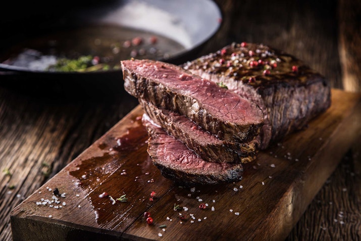 Sliced steak with seasoning on a wooden board.
