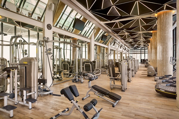 Luma Health Club, Grand Hyatt Spacious gym interior featuring modern fitness machines, mirrored walls, and a geometric ceiling design, providing a luxurious workout atmosphere.