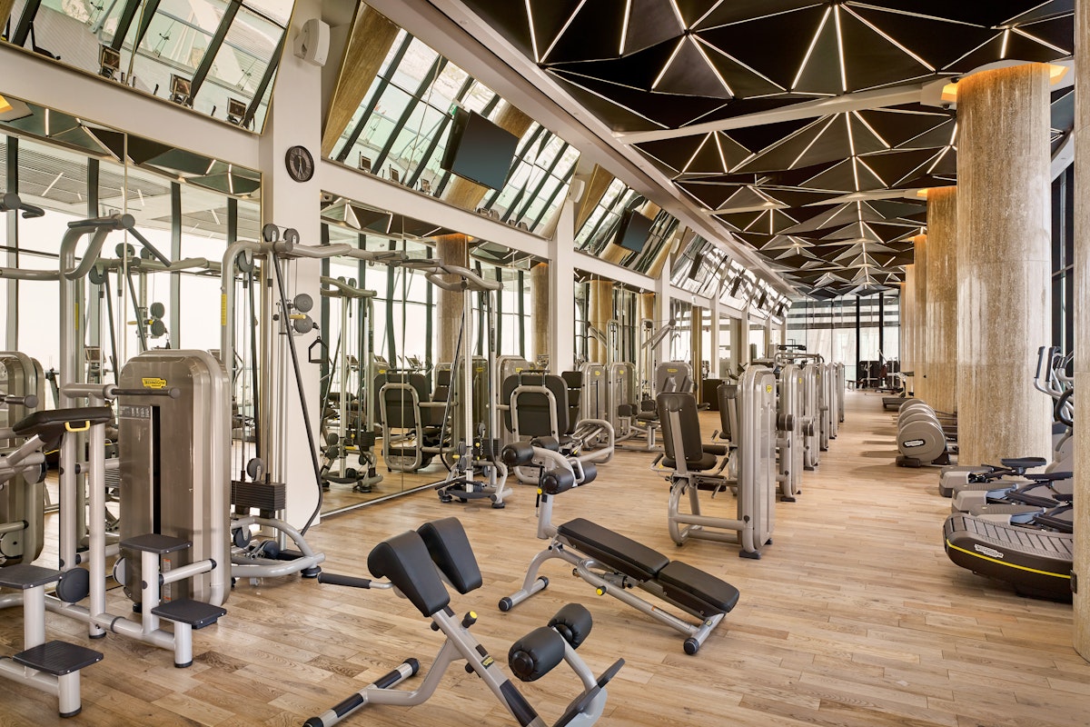 Luma Health Club, Grand Hyatt Spacious gym interior featuring modern fitness machines, mirrored walls, and a geometric ceiling design, providing a luxurious workout atmosphere.