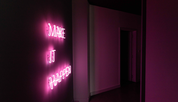 MOTION Cycling A pink neon sign on a dark wall reading 'MAKE IT HAPPEN,' illuminating a dimly lit hallway with a vibrant glow. The neon light creates an inspiring and motivational ambiance, urging action and positivity