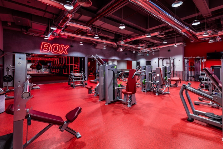 A red-themed gym with various workout machines and equipment, including a "BOX" sign on the wall.
