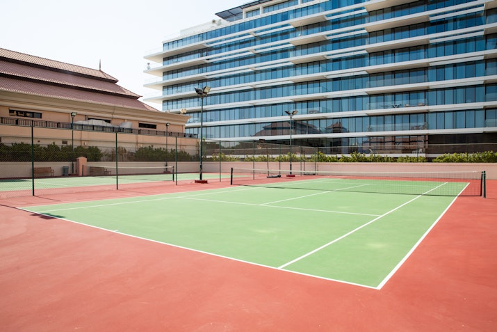 Tennis court with a red and green surface, surrounded by a modern building.