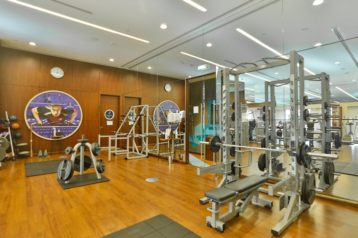 Modern gym with mirrored walls and wooden floors featuring various exercise machines and a spacious layout.