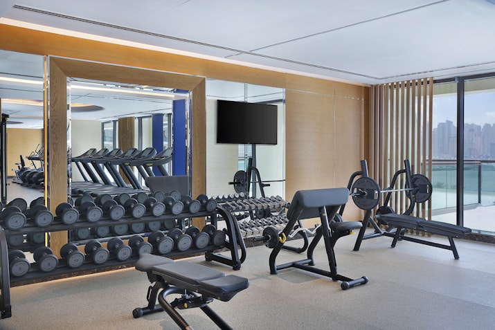 A modern gym interior featuring dumbbells, exercise equipment, and large windows overlooking a city view.