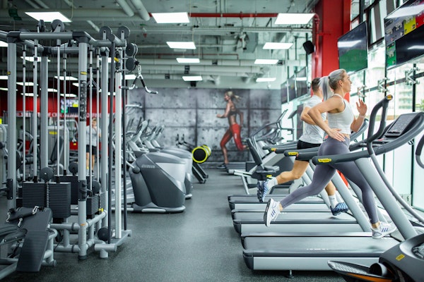View of a gym featuring treadmills and strength training equipment, with two people running on treadmills
