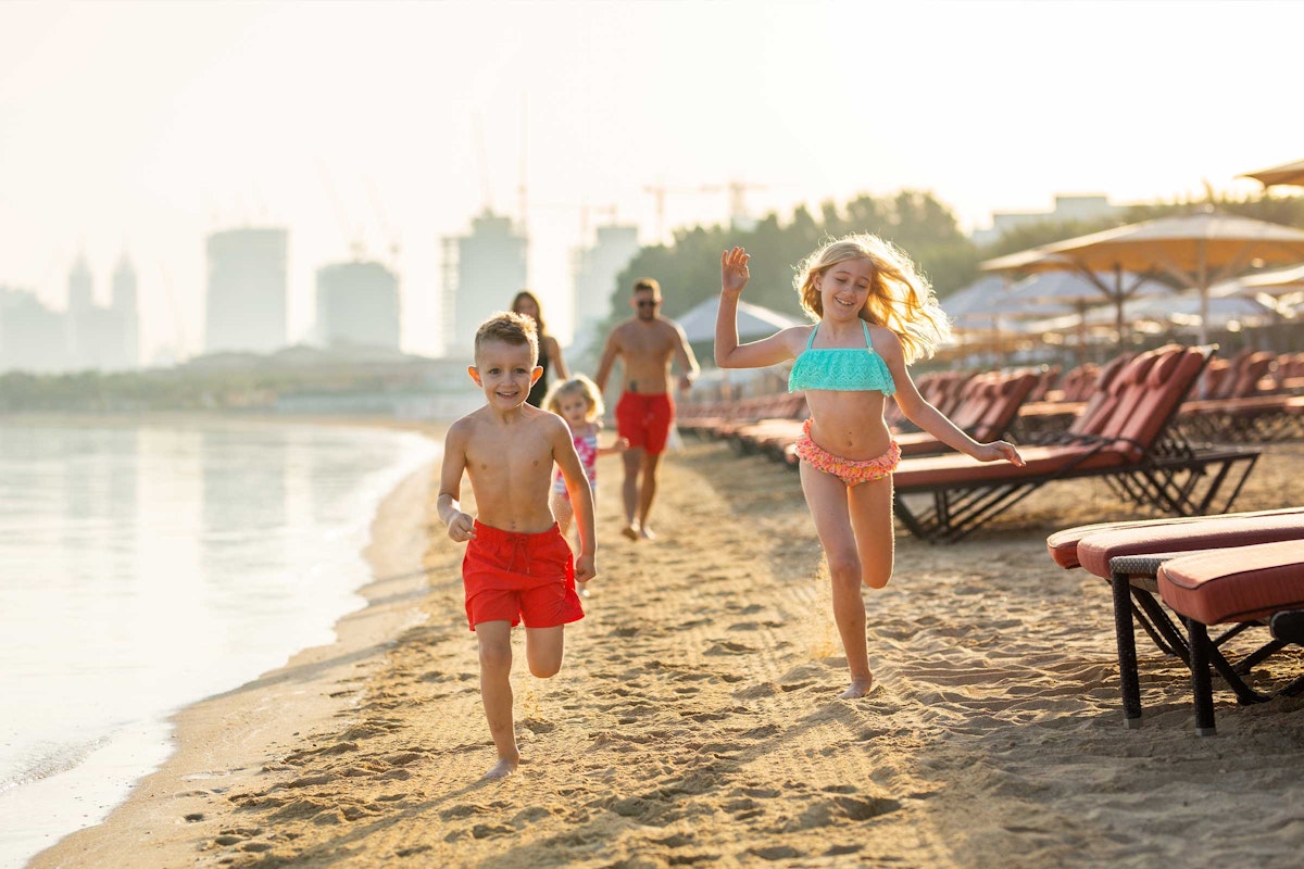 Children running on the beach with lounge chairs and umbrellas in the background.