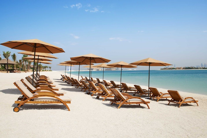 Sofitel Dubai The Palm Wooden lounge chairs with umbrellas on a sandy beach