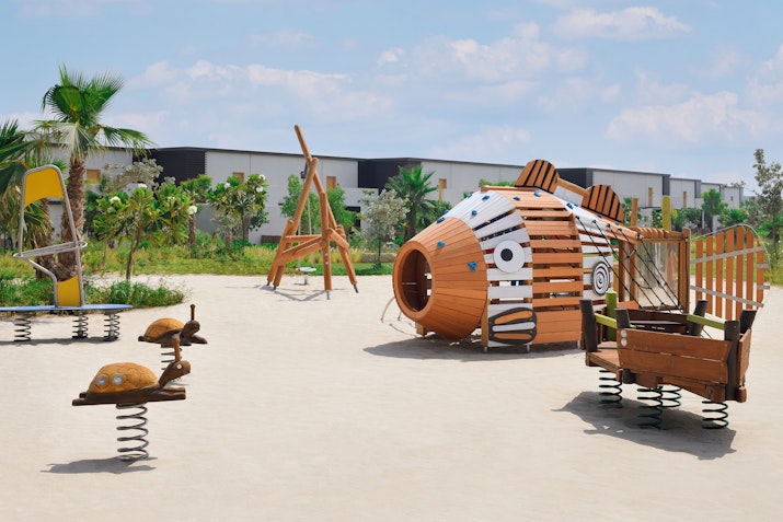 Mövenpick Resort Al Marjan Island A colorful outdoor playground featuring a fish-shaped play structure and spring riders, surrounded by greenery.
