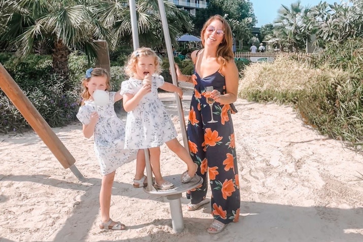 Mövenpick Resort Al Marjan Island A woman and two young girls smiling and posing together near a playground, with the woman standing on a swing set.