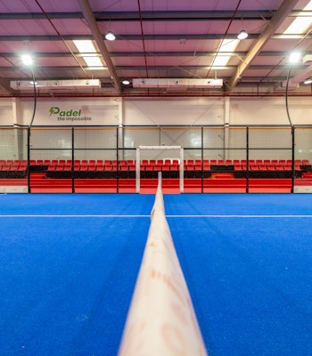Play padel indoors at Padelae Dubai Indoor paddle tennis court with vibrant blue flooring and red seating.