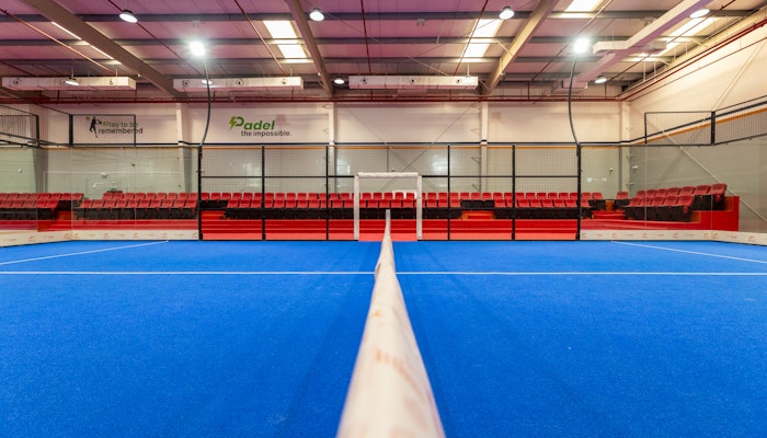 Play padel indoors at Padelae Dubai Indoor paddle tennis court with vibrant blue flooring and red seating.
