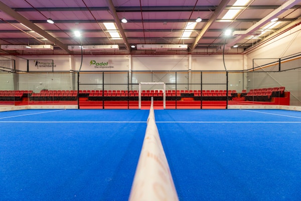 Indoor paddle tennis court with vibrant blue flooring and red seating.