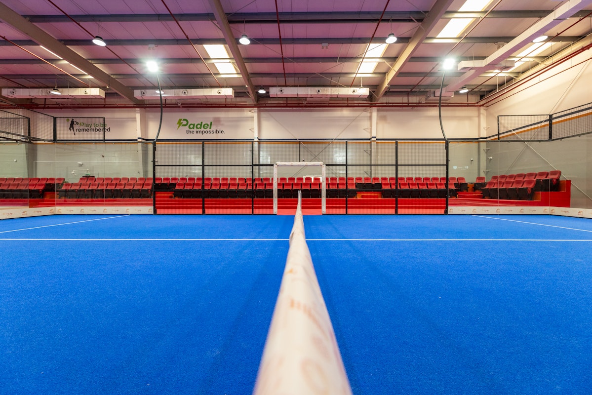 Indoor paddle tennis court with vibrant blue flooring and red seating.
