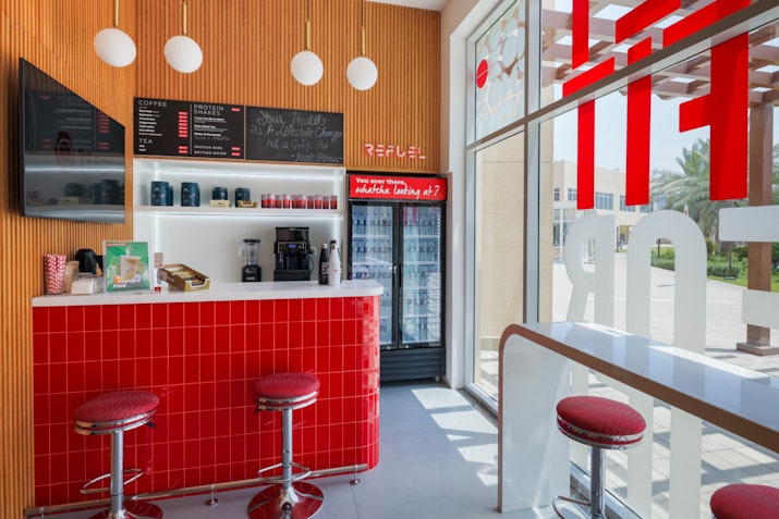 Interior view of a modern café featuring a red counter, bar stools, and a menu board.